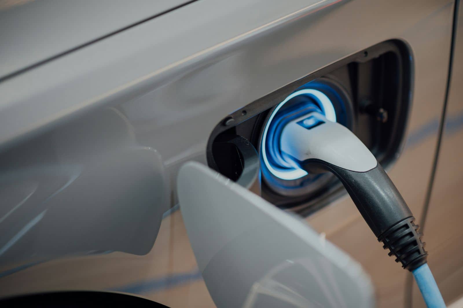 Close-up of a silver car's charge port with a glowing blue ring around the plugged-in connector